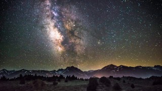 The milky way above a foggy landscape with mountains in the background and a forest in the foreground.